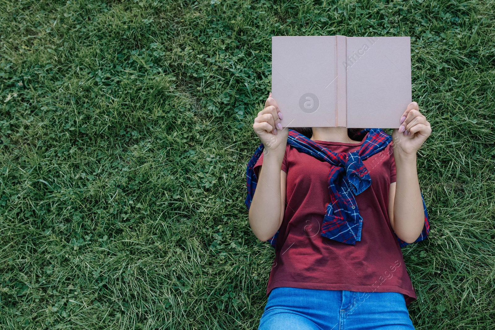 Photo of Woman reading book while lying on green grass outdoors, top view