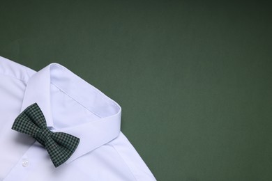 White shirt with stylish checkered bow tie on green background, top view. Space for text