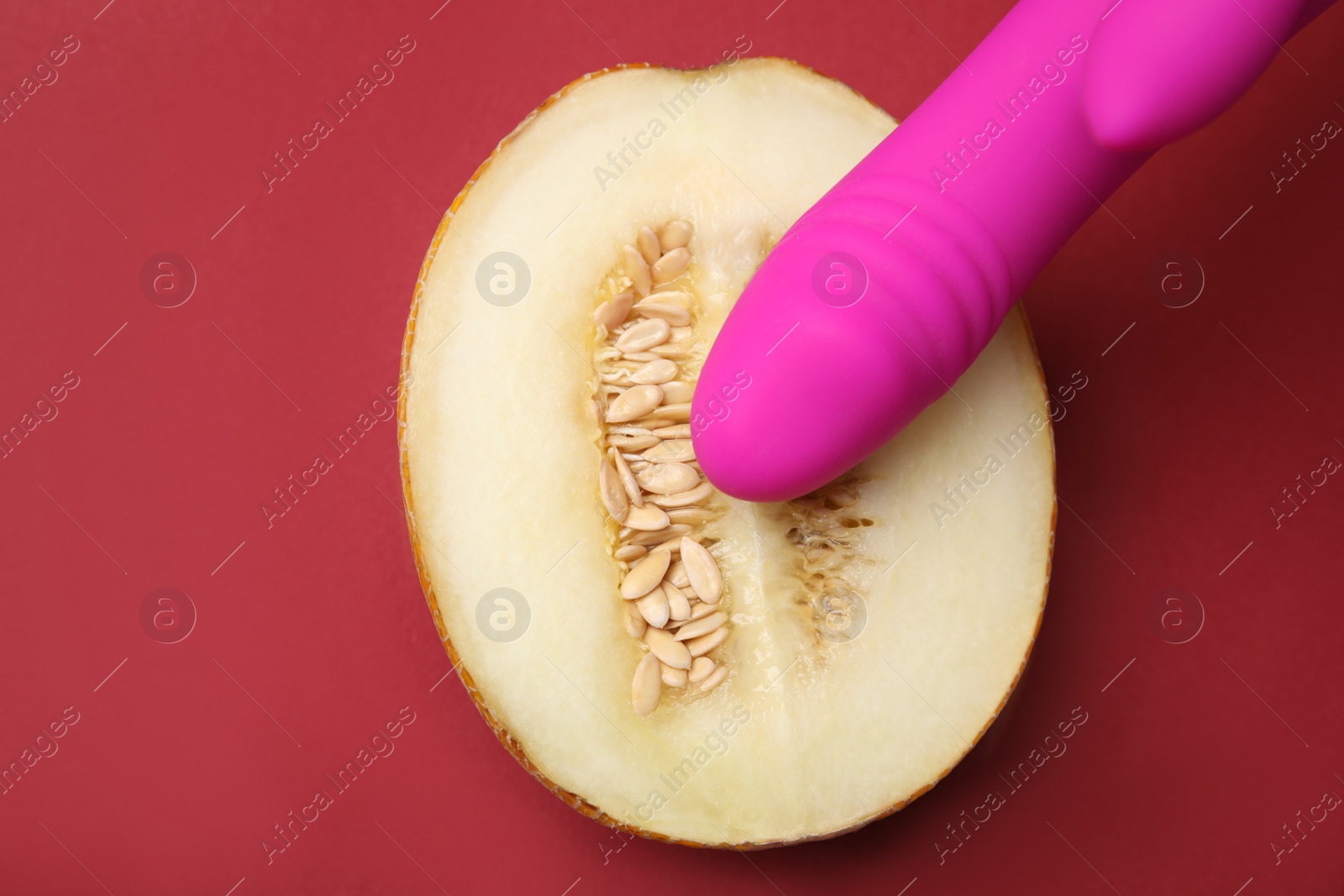 Photo of Half of melon and purple vibrator on red background, flat lay. Sex concept