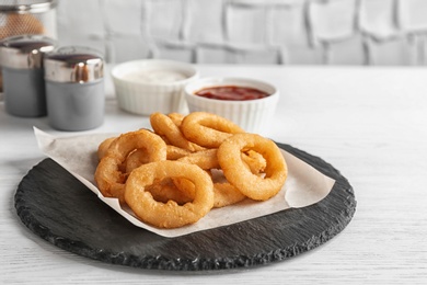 Photo of Slate plate with tasty onion rings on table