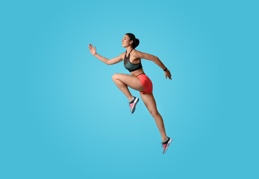 Photo of Athletic young woman running on light blue background, side view