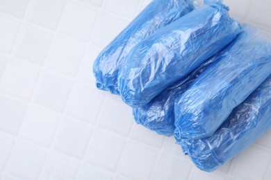 Rolled blue shoe covers on white tiled table, top view. Space for text