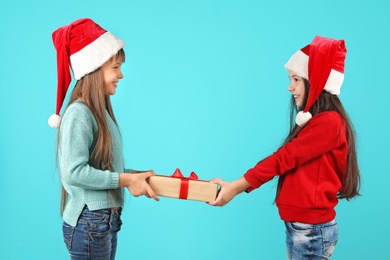 Photo of Cute little children in Santa hats with Christmas gift on color background