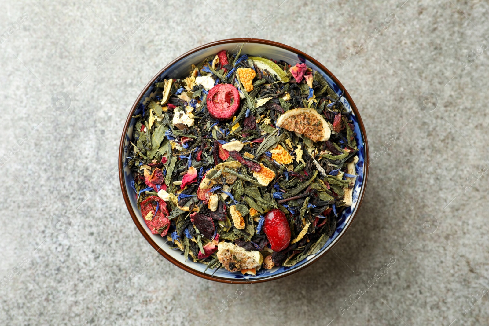 Photo of Bowl with dry herbal tea on grey table, top view