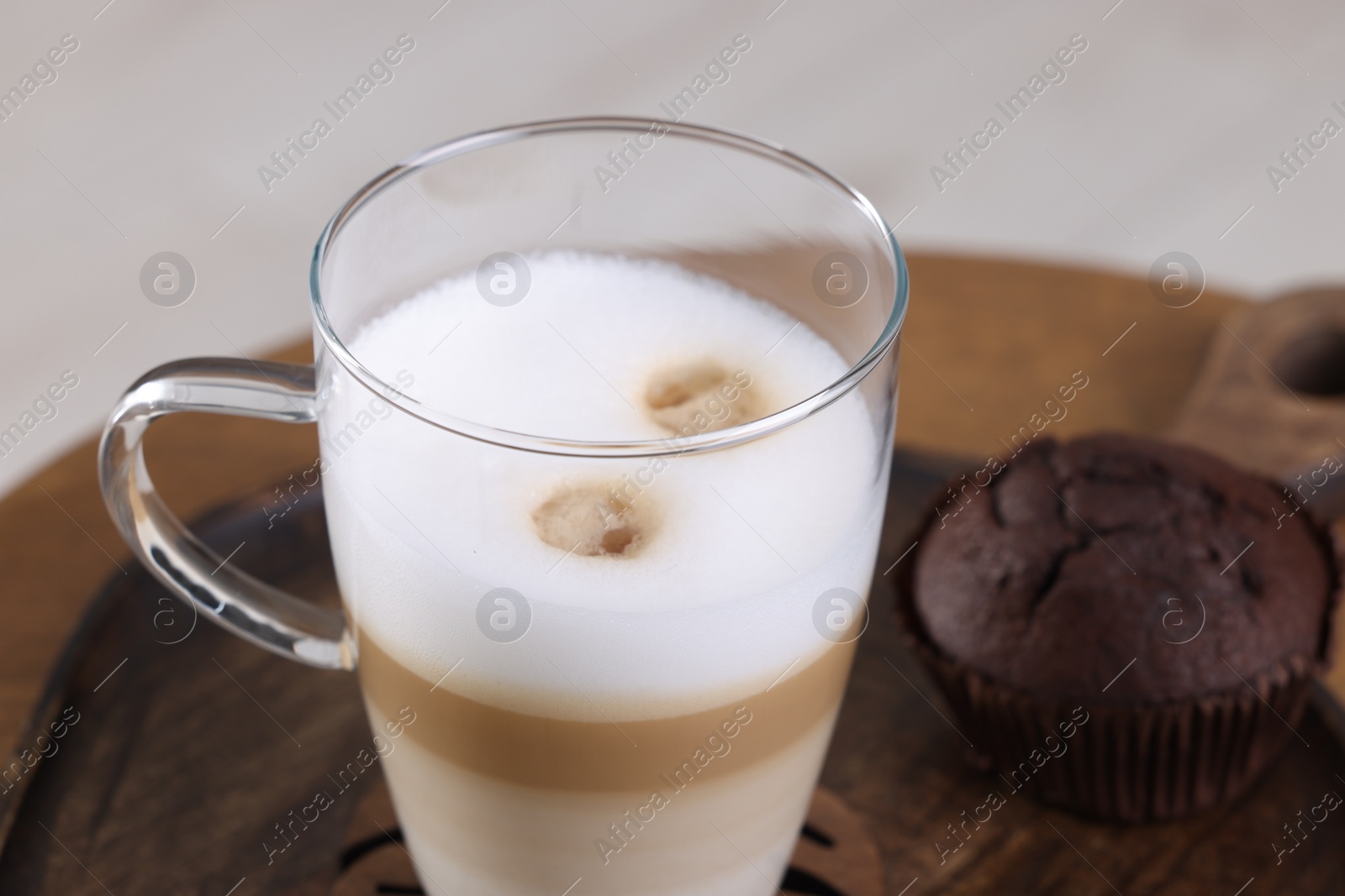 Photo of Cup of aromatic latte macchiato and chocolate muffin on table, closeup