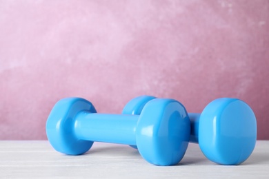 Stylish dumbbells on table against color background, space for text. Home fitness