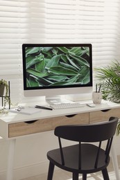 Photo of Comfortable workplace with modern computer and green plant in room. Interior design