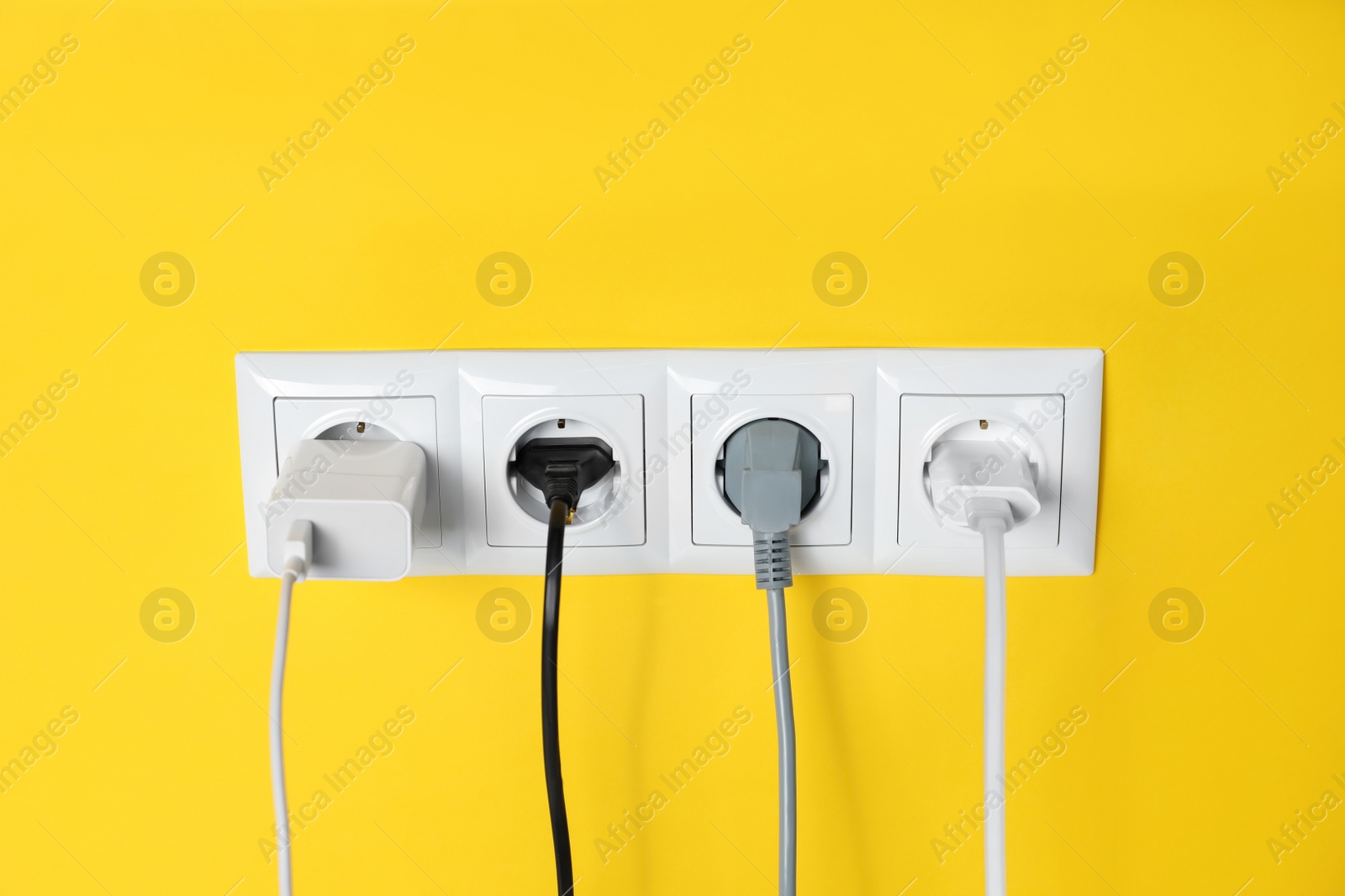 Photo of Power sockets with inserted plugs on yellow wall. Electrical supply