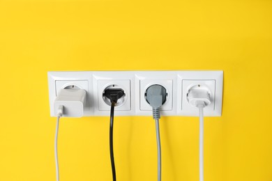 Photo of Power sockets with inserted plugs on yellow wall. Electrical supply