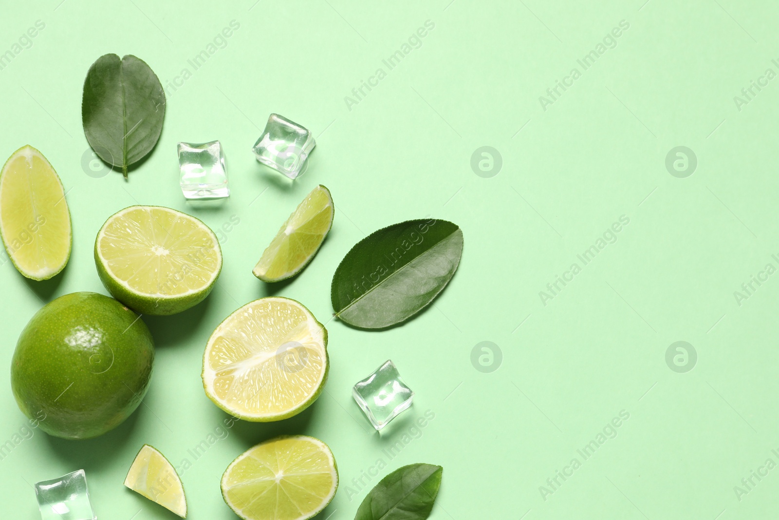 Photo of Fresh ripe limes with leaves and ice cubes on light green background, flat lay