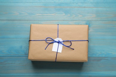 Photo of Parcel wrapped in kraft paper with tag on light blue wooden table, top view