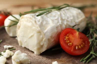 Photo of Delicious goat cheese with tomato and rosemary on wooden board, closeup