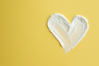 Photo of Samples of face cream in shape of heart on yellow background, top view. Space for text