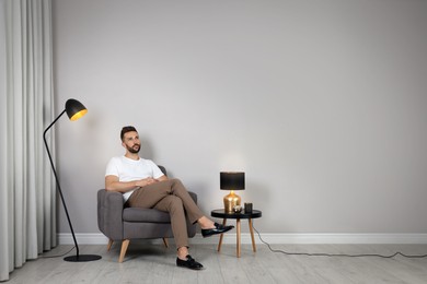 Man sitting in armchair near gray wall, space for text