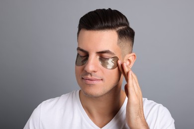 Photo of Man applying dark under eye patch on grey background