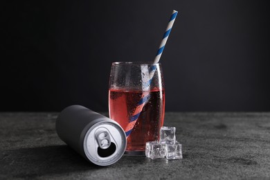 Photo of Energy drink in glass, aluminium can and ice cubes on grey table