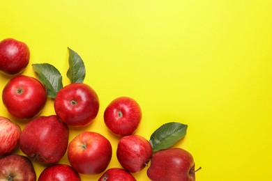 Ripe red apples and green leaves on yellow background, flat lay. Space for text