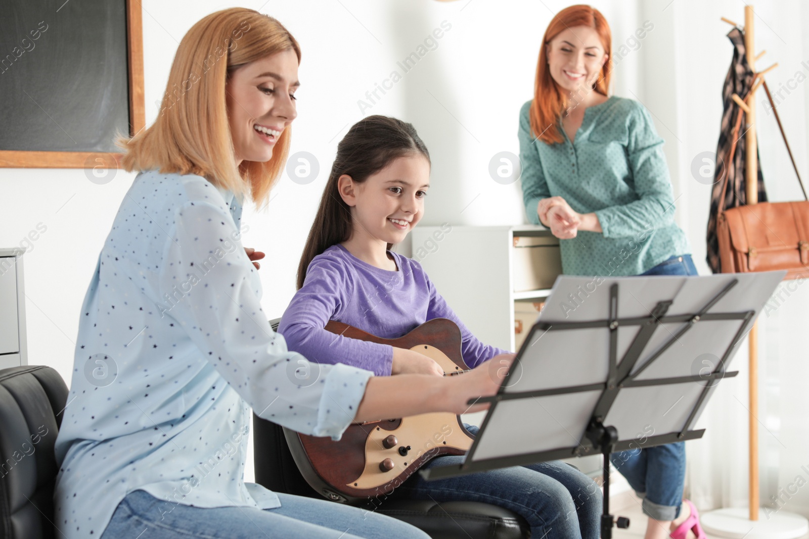 Photo of Little girl with her teacher and mother at music lesson. Learning notes