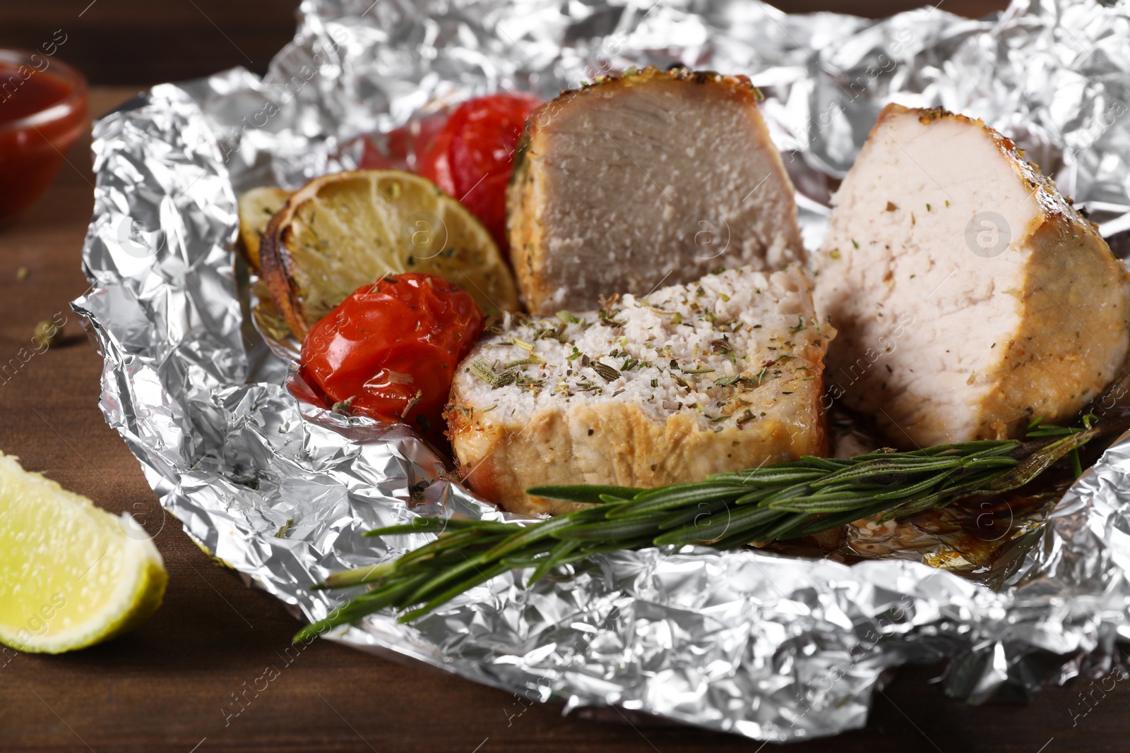 Photo of Pieces of delicious meat baked in foil with tomatoes on wooden table, closeup