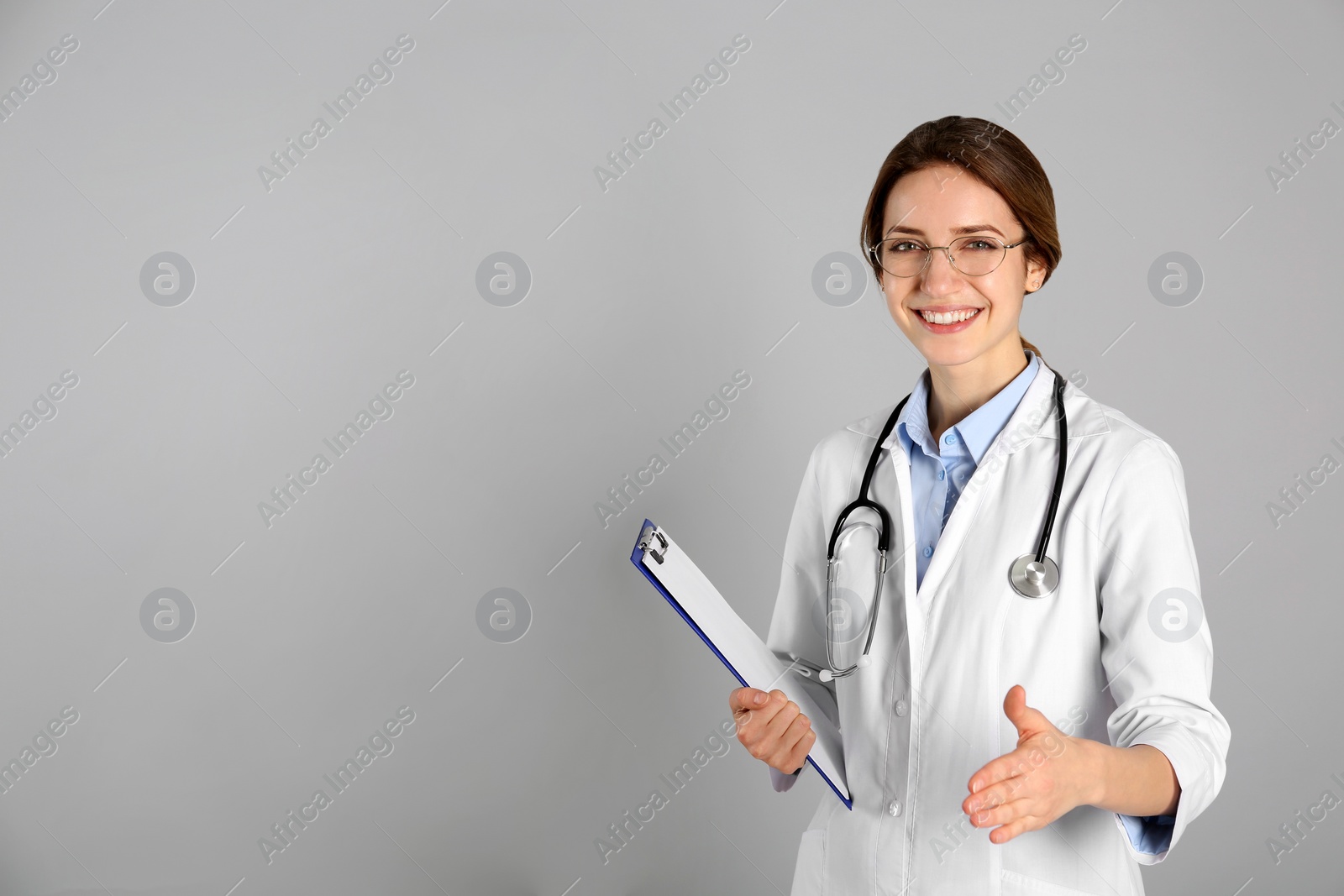 Photo of Happy female doctor offering handshake on light grey background. Space for text