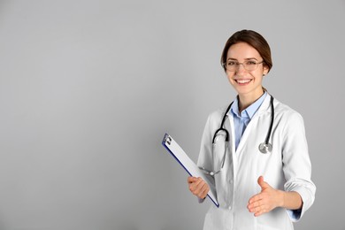 Photo of Happy female doctor offering handshake on light grey background. Space for text