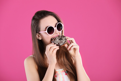 Photo of Beautiful young woman wearing sunglasses with donut on pink background