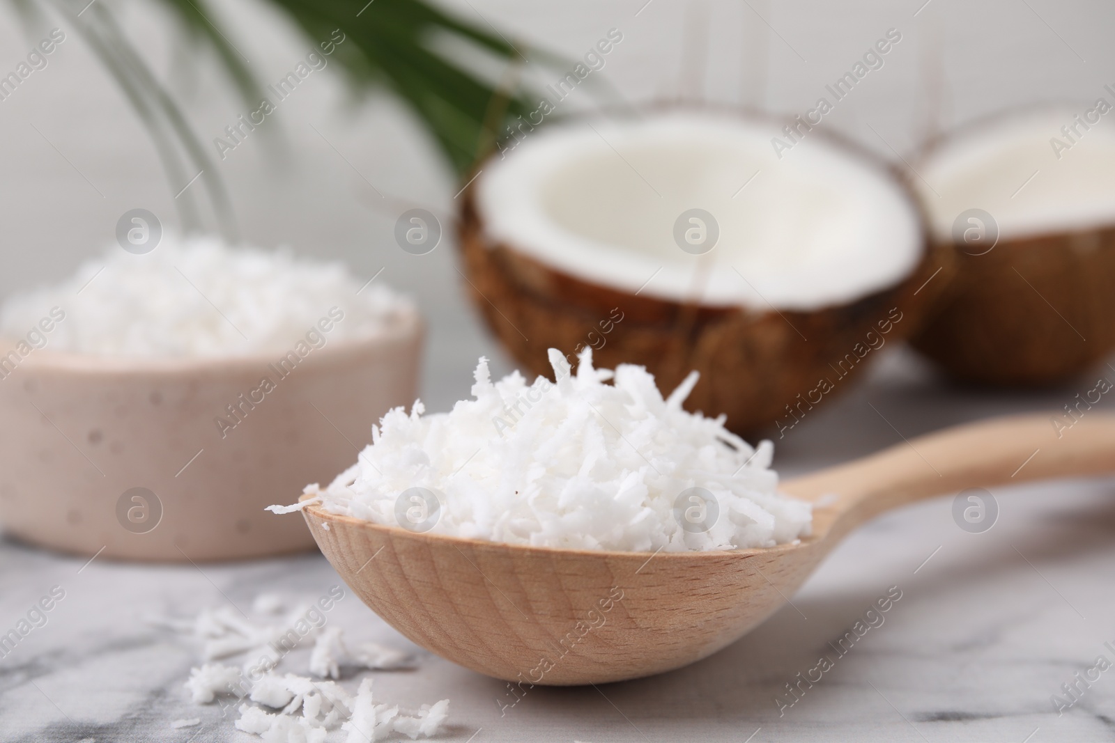 Photo of Coconut flakes in wooden spoon on white marble table, closeup