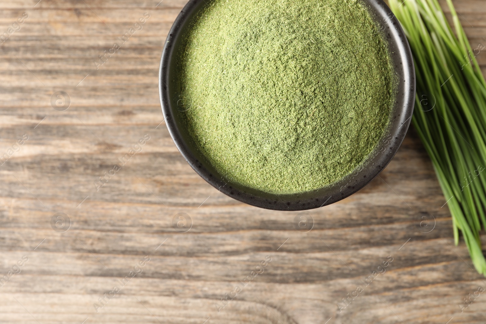 Photo of Wheat grass powder in bowl and fresh sprouts on wooden table, flat lay. Space for text