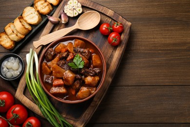 Photo of Delicious beef stew with carrots, parsley and potatoes on wooden table, flat lay. Space for text