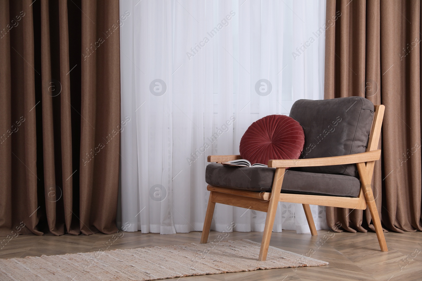 Photo of Comfortable armchair with cushion near window indoors, space for text. Interior design