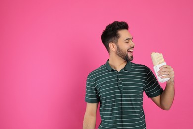 Young man eating tasty shawarma on pink background. Space for text