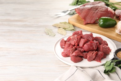 Photo of Plate with pieces of raw beef meat, spices and products on light wooden table. Space for text