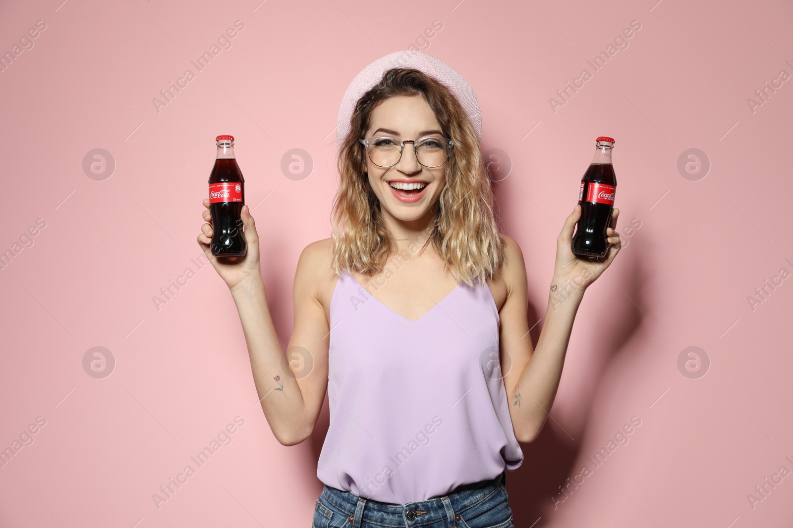 Photo of MYKOLAIV, UKRAINE - NOVEMBER 28, 2018: Young woman with bottles of Coca-Cola on color background