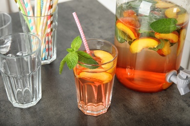 Photo of Peach cocktail in glass and jar with tap on table. Refreshing drink