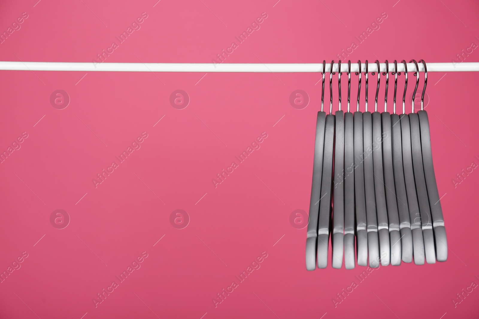 Photo of Empty clothes hangers on metal rail against color background. Space for text