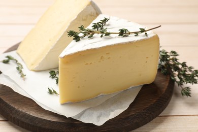 Photo of Board with pieces of tasty camembert cheese and thyme on light wooden table, closeup