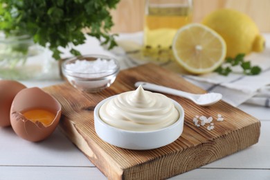 Photo of Fresh mayonnaise sauce in bowl and ingredients on white wooden table