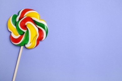 Photo of Stick with colorful lollipop swirl on violet background, top view. Space for text