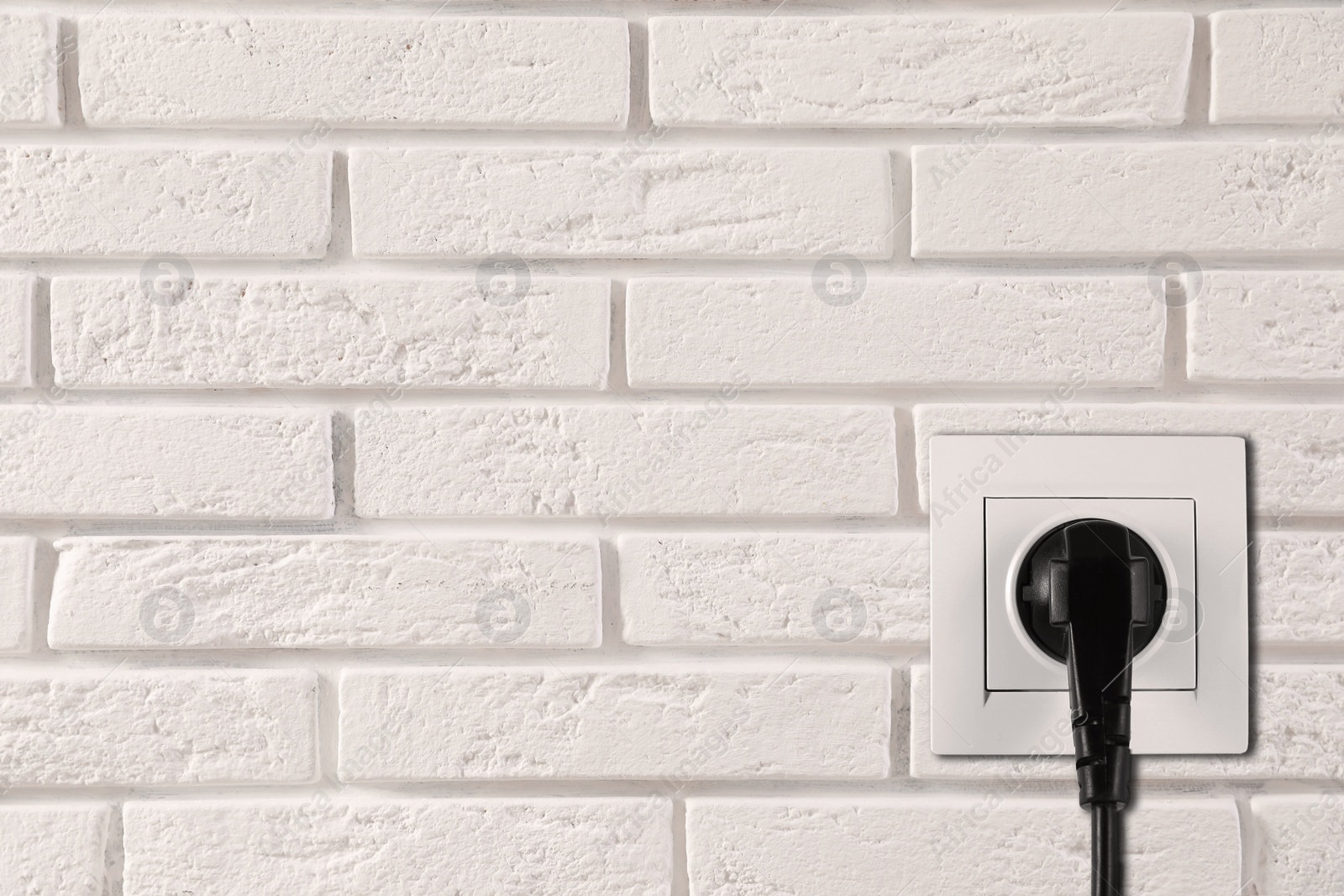 White brick wall with power socket and inserted plug, space for text. Electrical supply Image of White brick wall with power socket and inserted plug, space for text. Electrical supply