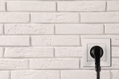 Image of White brick wall with power socket and inserted plug, space for text. Electrical supply
