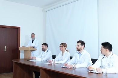 Photo of Senior doctor giving lecture in conference room with projection screen