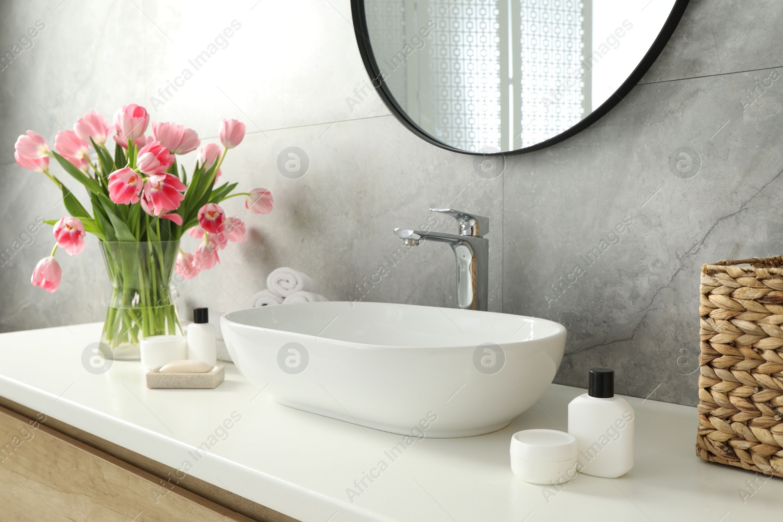 Photo of Vase with beautiful pink tulips and toiletries near sink in bathroom