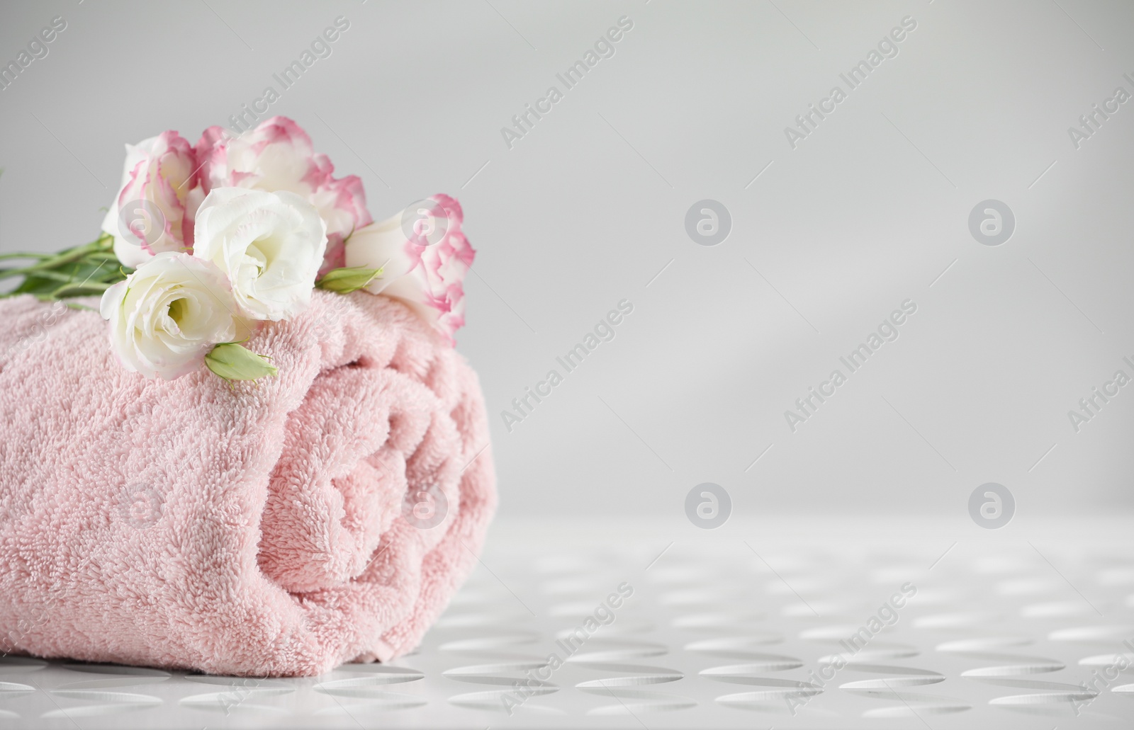 Photo of Rolled soft towel and eustoma flowers on white table, space for text