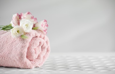 Photo of Rolled soft towel and eustoma flowers on white table, space for text