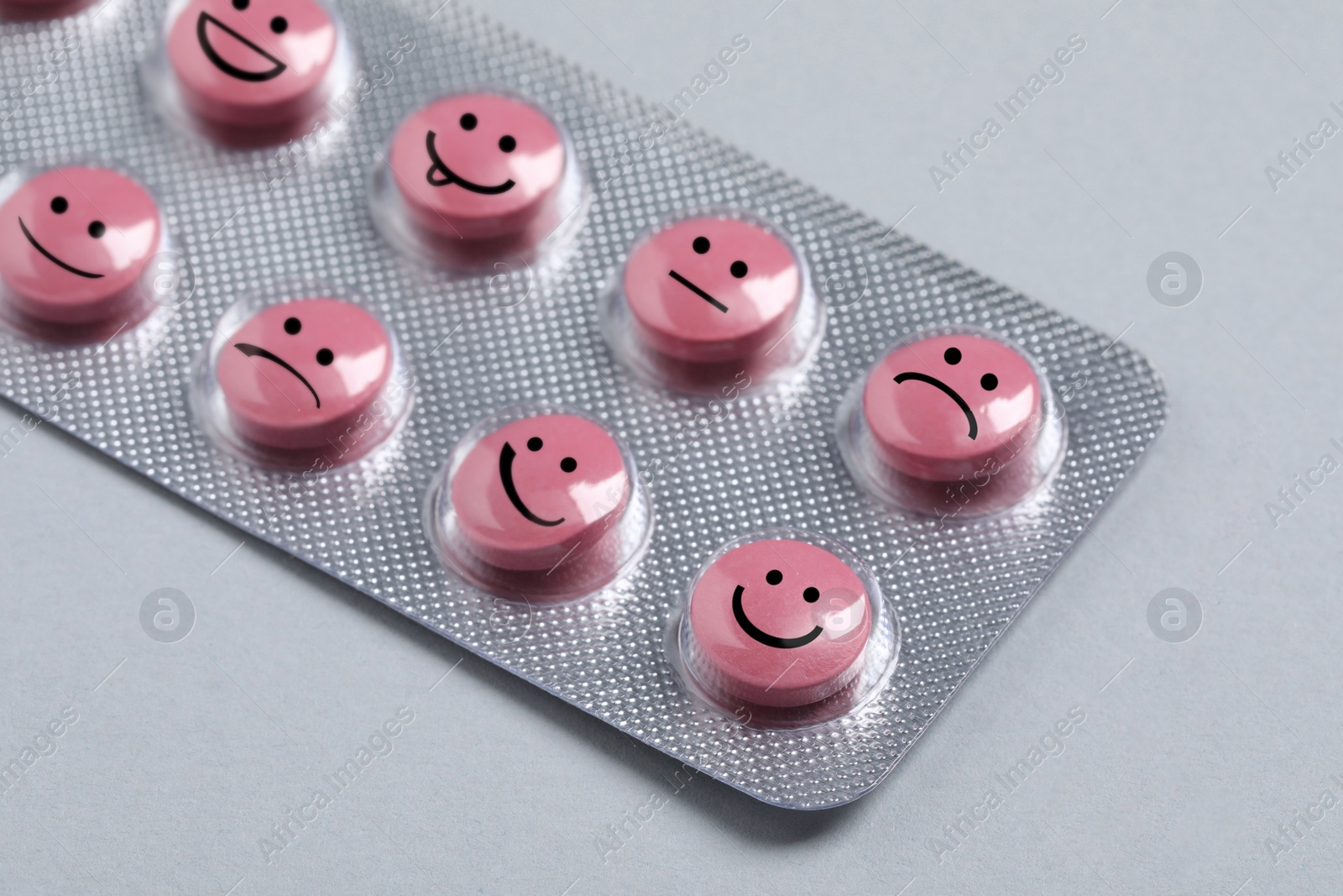 Image of Pink pills with different emotional faces in blister on light grey background