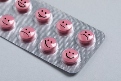 Image of Pink pills with different emotional faces in blister on light grey background