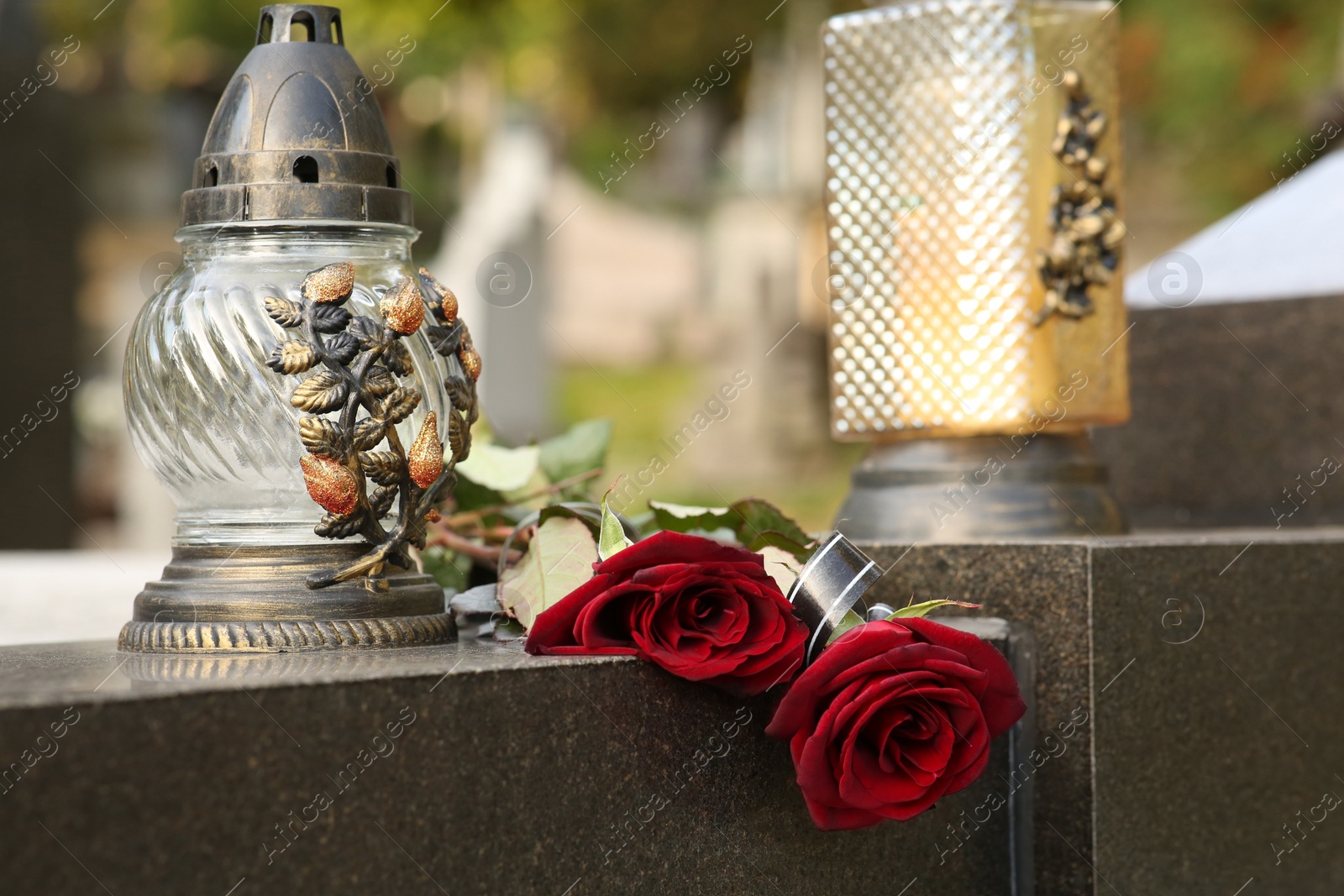 Photo of Red roses and grave light on grey granite tombstone outdoors. Funeral ceremony