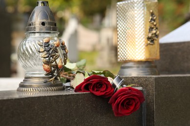 Photo of Red roses and grave light on grey granite tombstone outdoors. Funeral ceremony