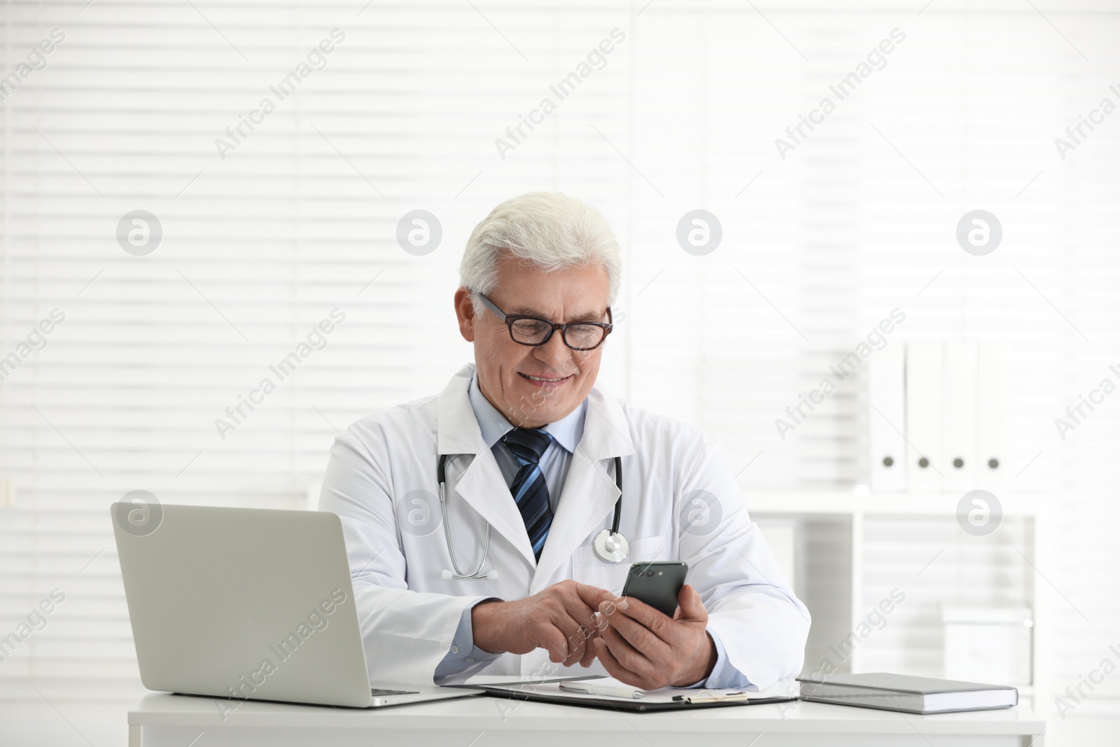 Photo of Senior doctor with smartphone at table in office