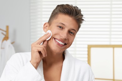 Photo of Handsome young man cleaning face with cotton pad in bathroom
